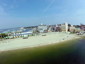 Un paisaje urbano costero con una amplia playa de arena, un puerto deportivo y diversos edificios, incluyendo un hotel destacado con una torre.