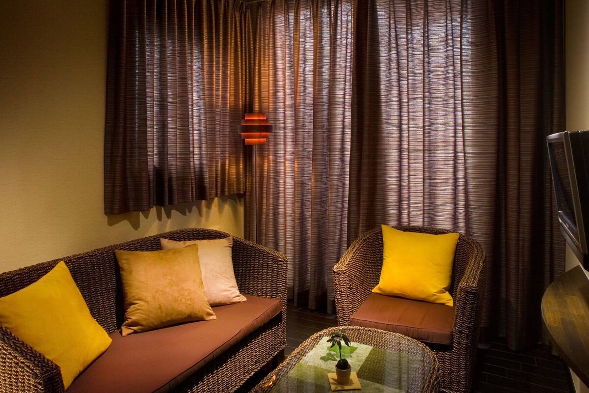 Un espacio de sala acogedor con un sofá, sillón y una mesa de centro, que destaca por un techo estampado y cortinas.