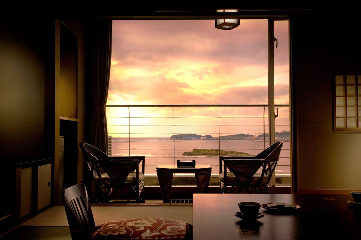 Una habitación con vista al mar, una mesa con sillas y una puerta corredera japonesa tradicional.