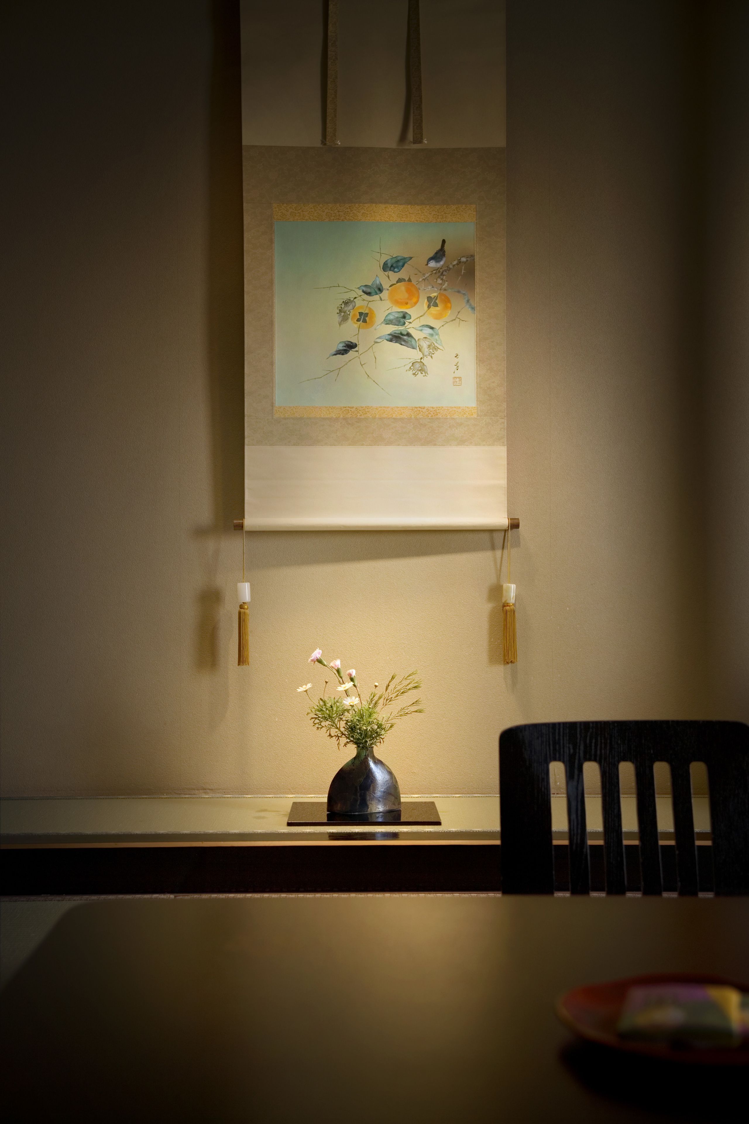 A dining table with a vase of flowers, a framed artwork above, and a chair.