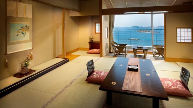 Une pièce de style japonais traditionnel, avec un sol recouvert de tatamis, une petite table basse entourée de coussins et une vue sur la mer.