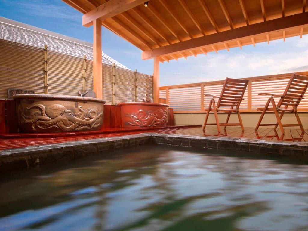A hot spring area with a wooden deck, two wooden chairs, and a stone basin with carved designs.