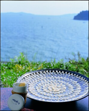 Ein Tisch mit einer verzierten Platte und einer Tasse, vor einer Kulisse aus Wasser und Grünpflanzen.