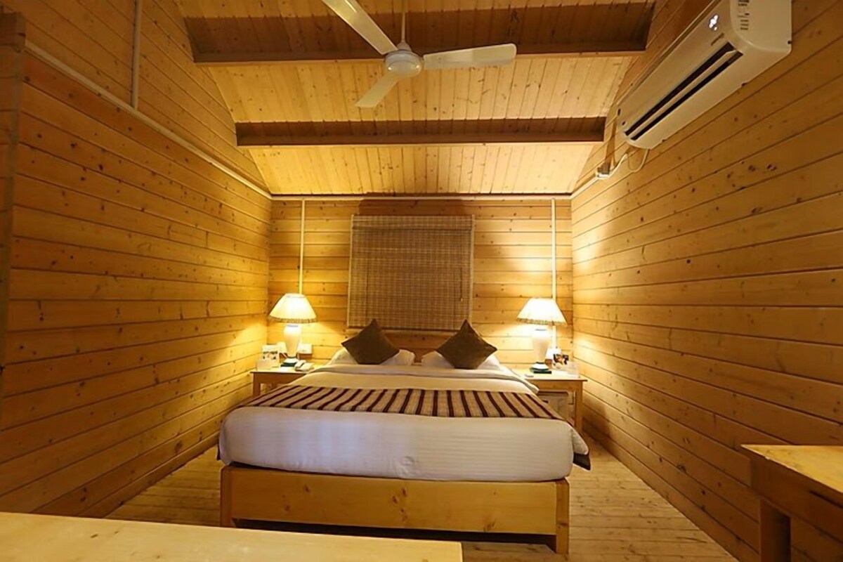 A wooden-paneled room with a bed, two bedside lamps, a ceiling fan, and an air conditioning unit.