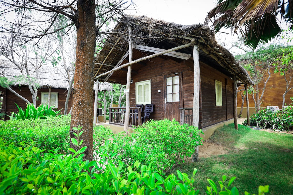 A wooden house with a thatched roof, surrounded by lush greenery and a well-maintained lawn.
