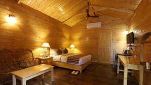 A wooden cabin with a bed, two lamps, a bench, a table, and a television. - Lotus an Eco Resort Konark (Gop)