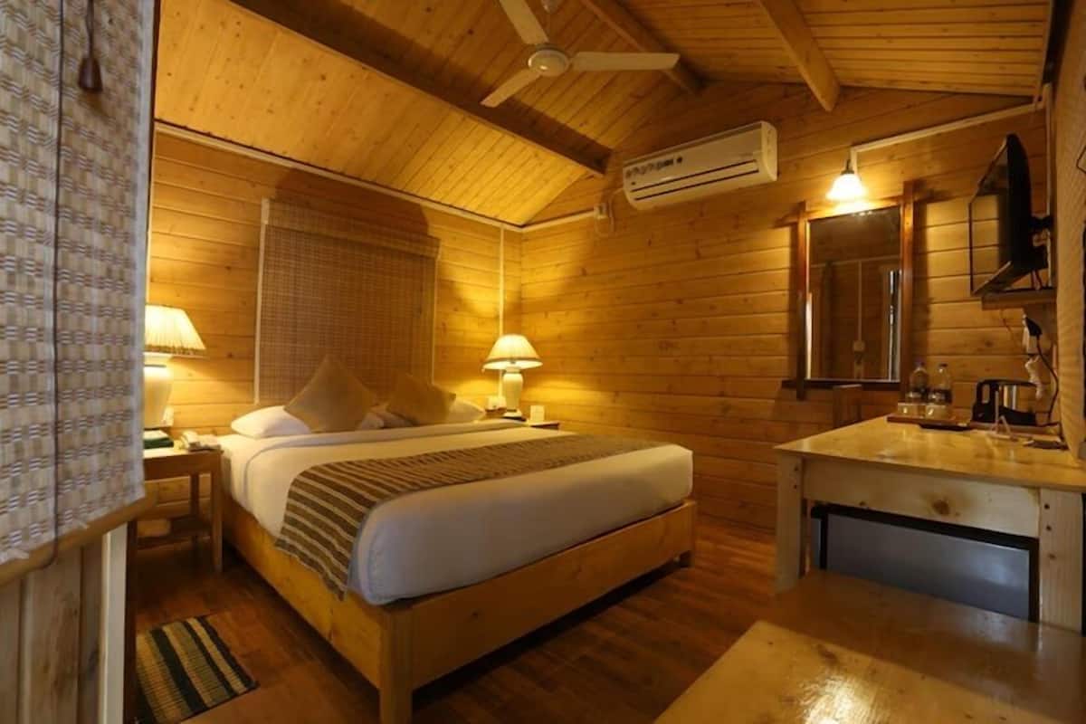 A wooden cabin room with a bed, bedside lamps, a wooden dresser, a mirror, and an air conditioning unit.