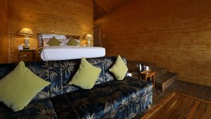 A wooden cabin room with a bed, a sofa, two lamps, and a small table. - Lotus an Eco Resort Konark (Gop)