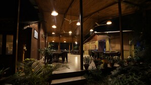 An indoor dining area with multiple tables and chairs, wooden ceiling beams, and potted plants. - Lotus an Eco Resort Konark (Gop)