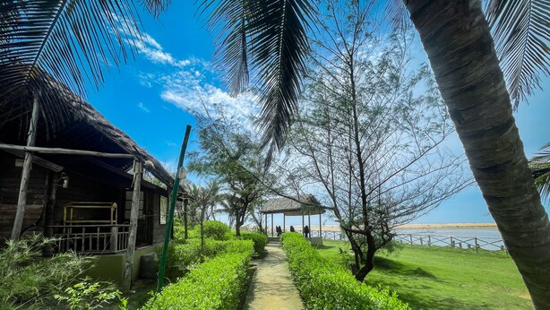 A pathway leading to a gazebo with a view of the sea, surrounded by lush greenery and palm trees. - Lotus an Eco Resort Konark (Gop)