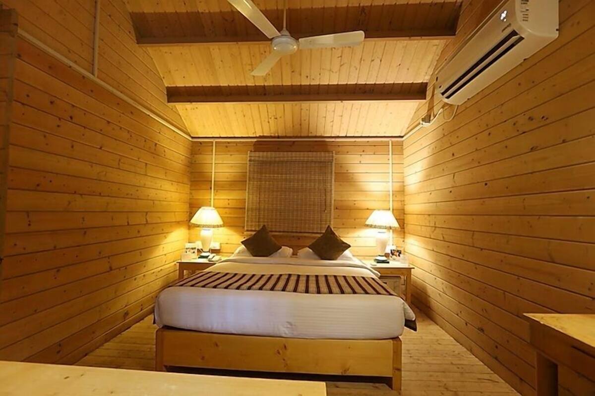 A wooden-paneled room with a bed, two bedside lamps, a ceiling fan, and an air conditioning unit.