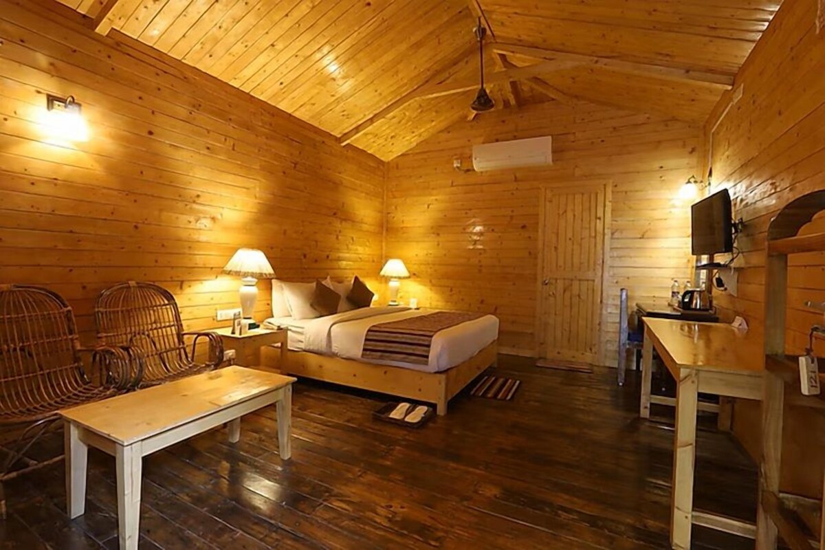 A wooden cabin interior with a bed, two chairs, a table, and a television.