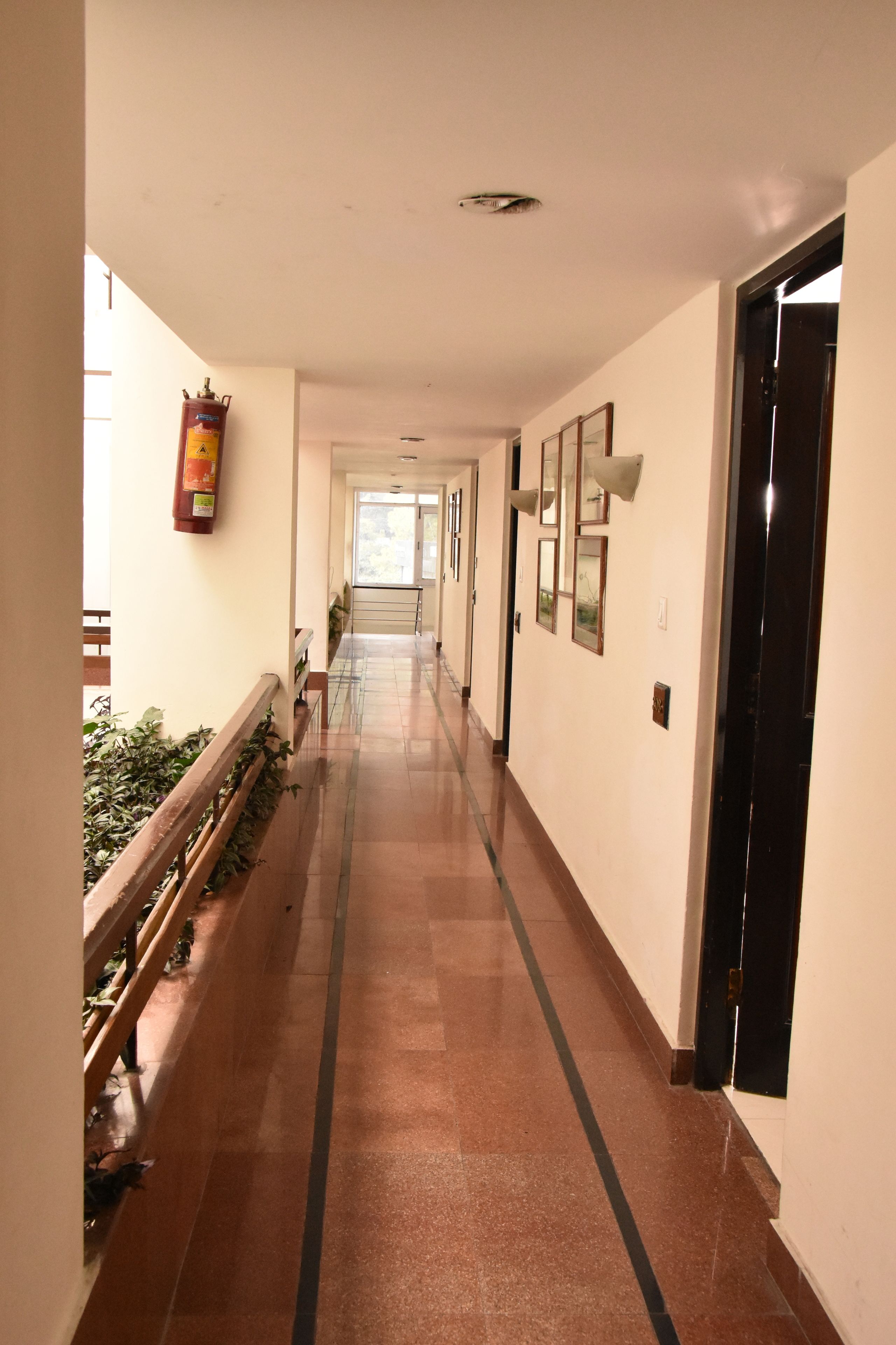 A long, narrow hallway with a tiled floor, a fire extinguisher mounted on the wall, and framed pictures on the right side.