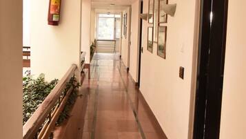 A long, narrow hallway with a tiled floor, a fire extinguisher mounted on the wall, and framed pictures on the right side.