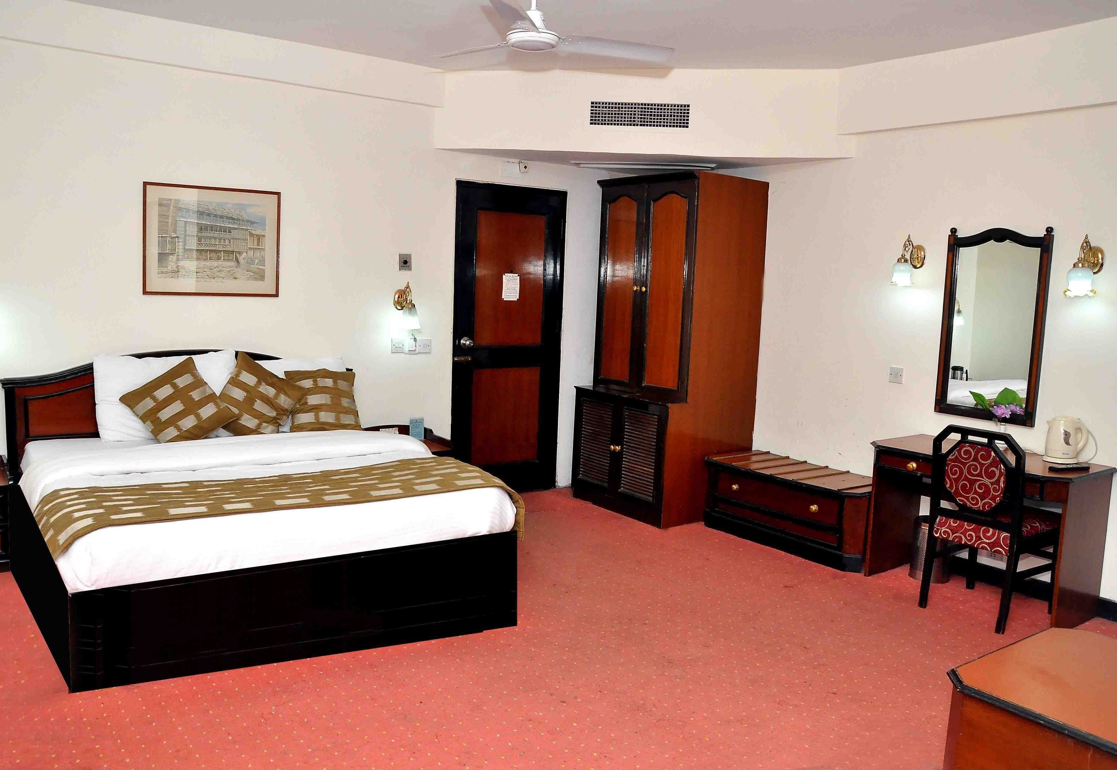 A bedroom with a bed, a desk, a chair, a wardrobe, and a mirror.