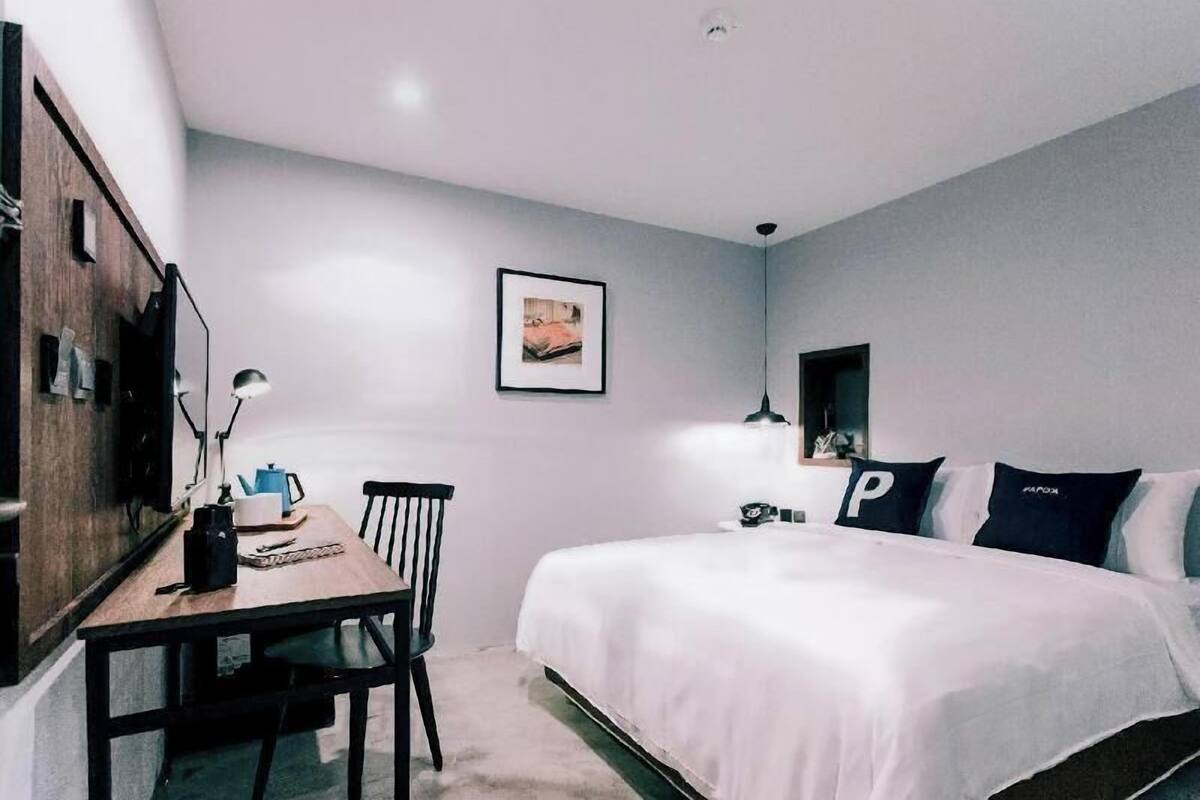 A bedroom with a bed, a desk, a chair, a lamp, and a framed picture on the wall.