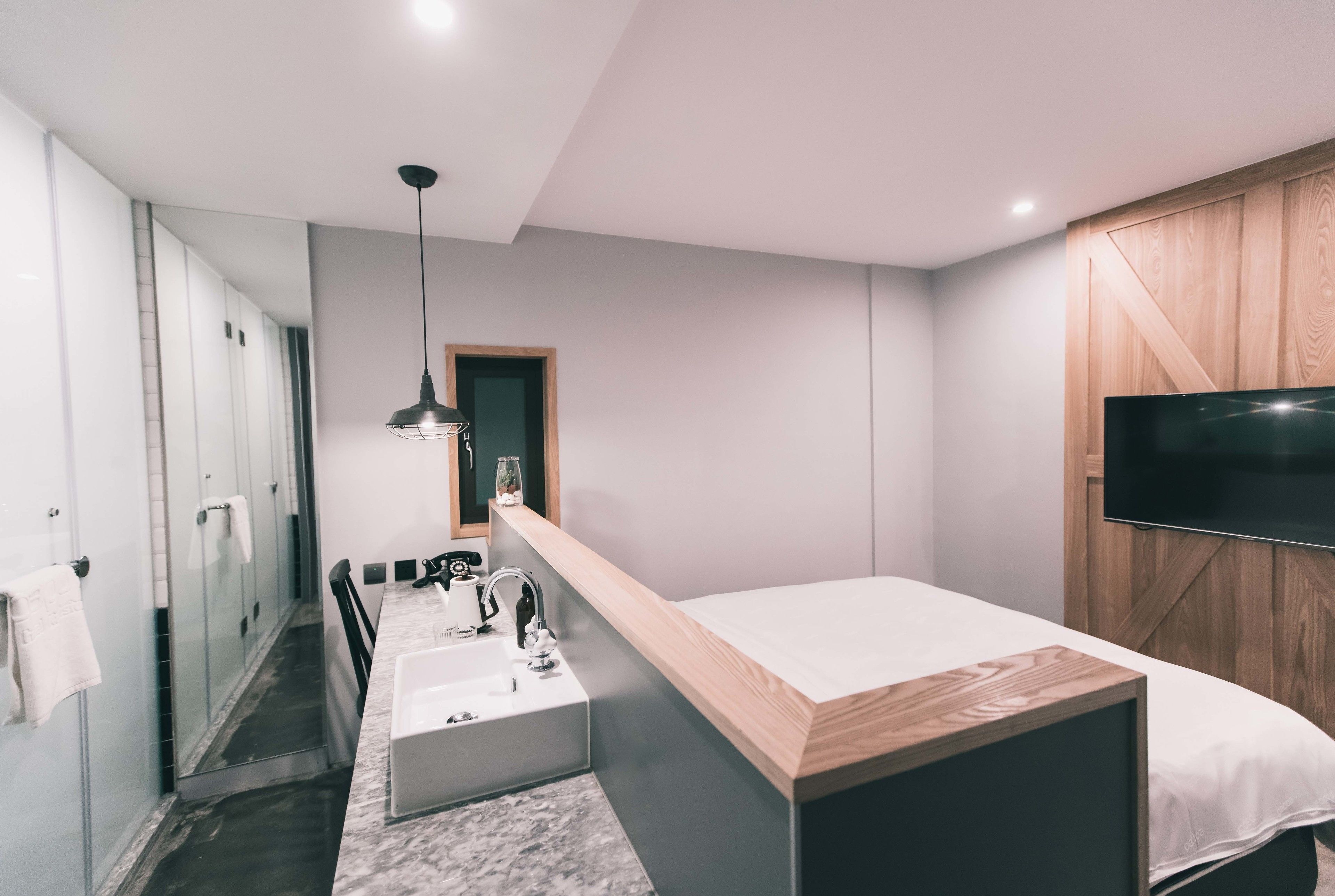 Une chambre d’hôtel moderne avec un lit en bois, un grand téléviseur fixé au mur, un lavabo intégré et un dressing avec des portes coulissantes.