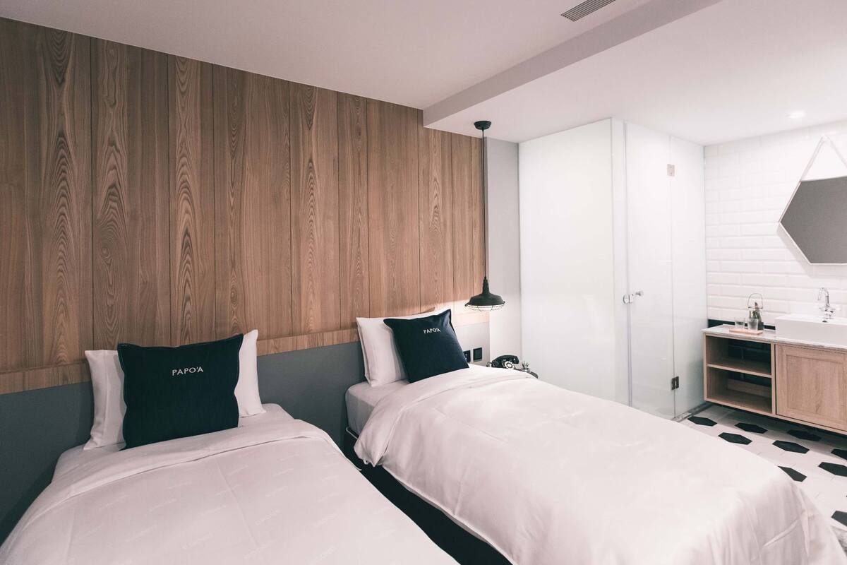 A hotel room with two beds, a wooden headboard, a white sink, and a mirror.