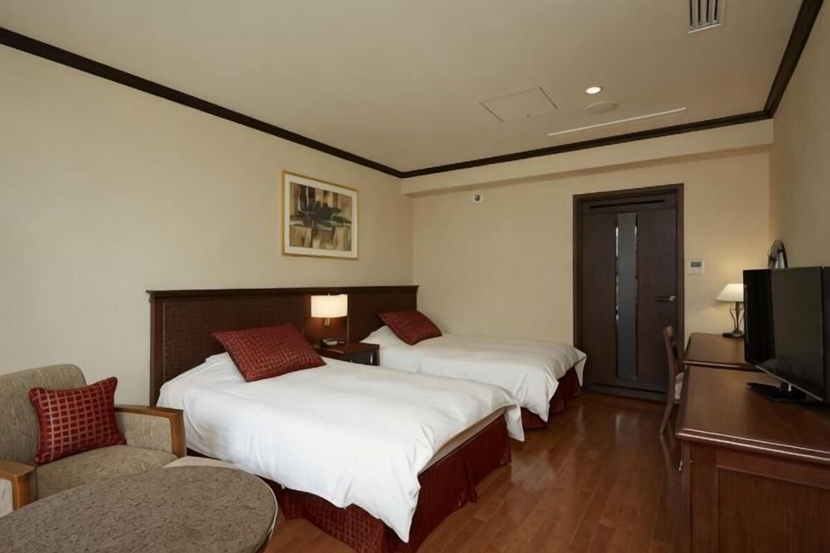 Ein Hotelzimmer mit zwei Betten, einem Fernseher, einem Schreibtisch und einem Sessel.