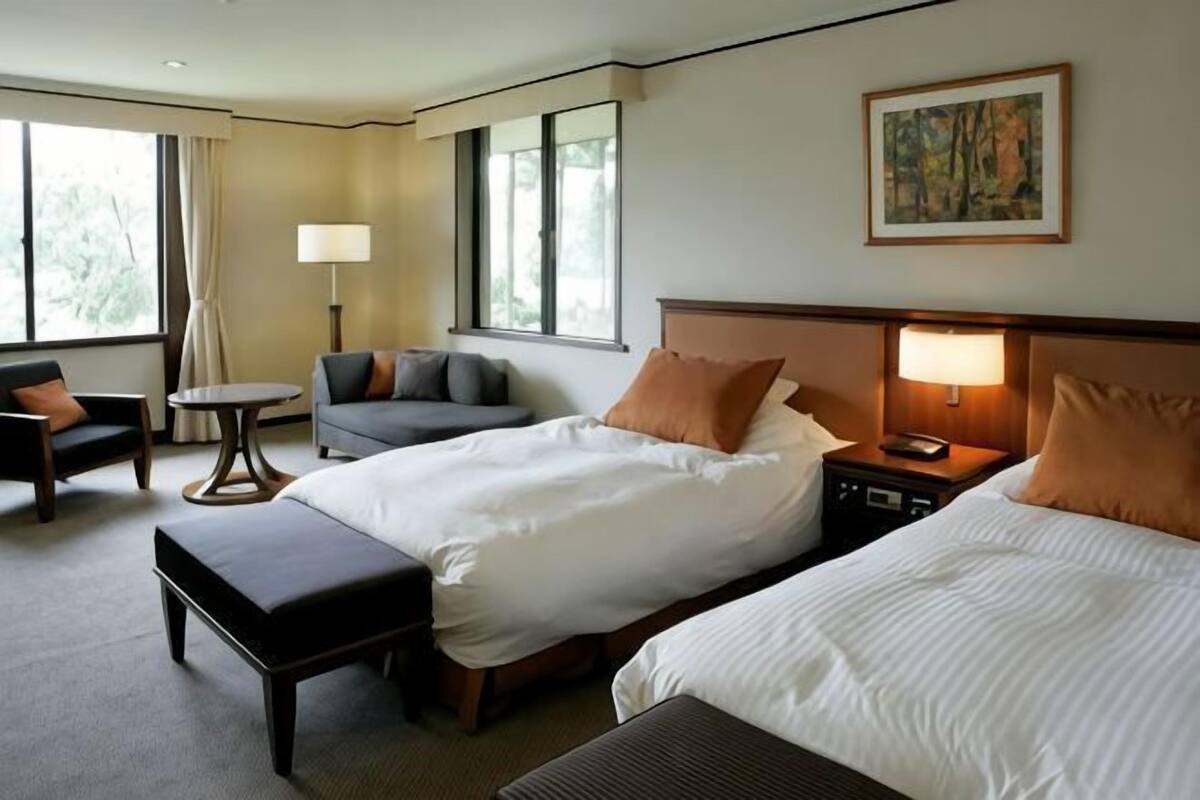 Habitación de hotel con dos camas, un escritorio, una silla, una lámpara y un cuadro en la pared.