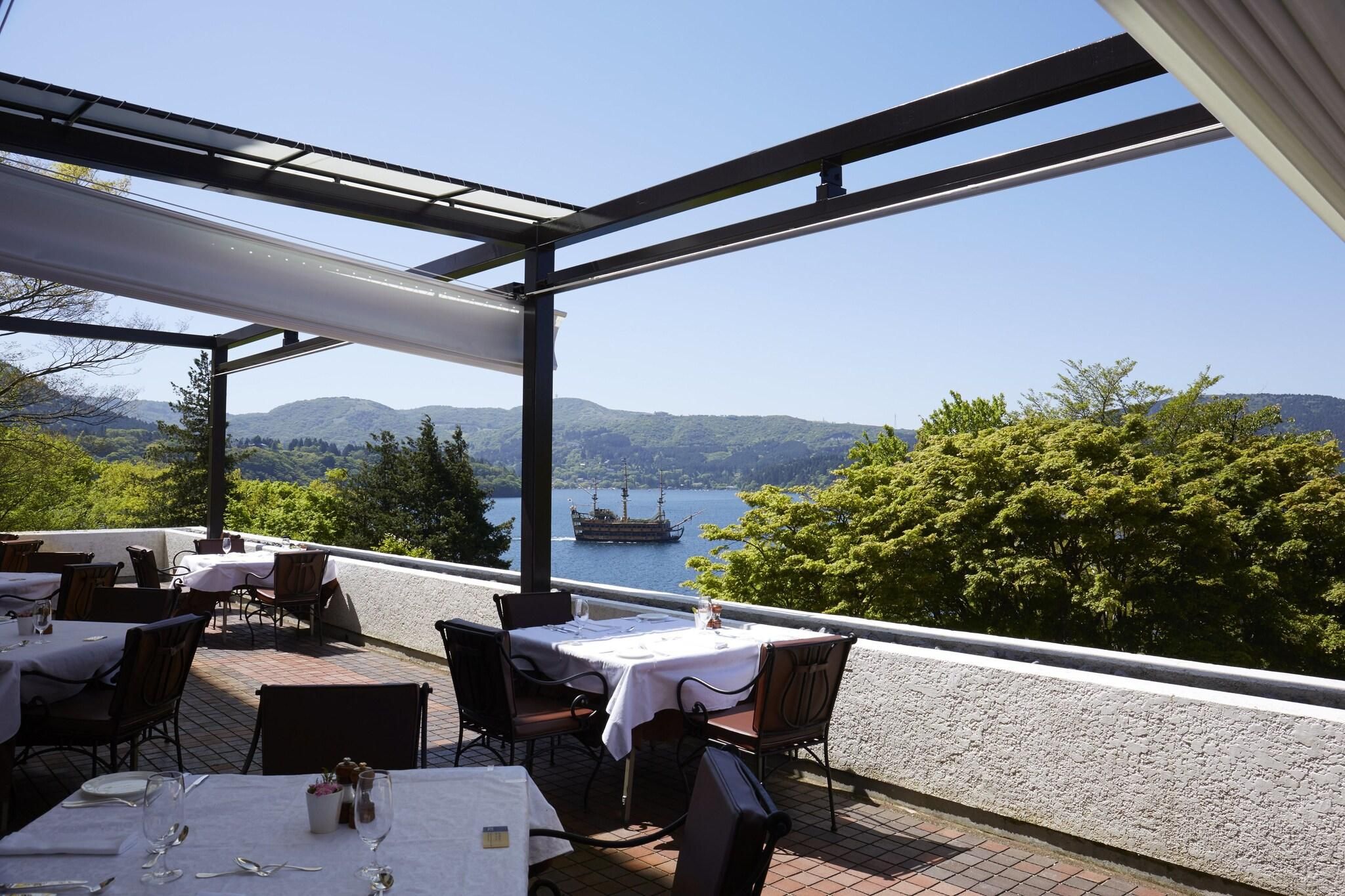 An outdoor dining area with tables and chairs, overlooking a lake and mountains.