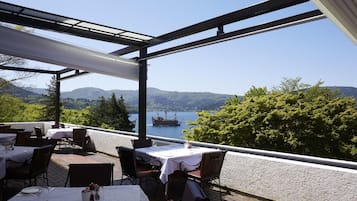 An outdoor dining area with tables and chairs, overlooking a lake and mountains.