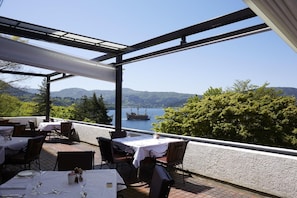 An outdoor dining area with tables and chairs, overlooking a lake and mountains.