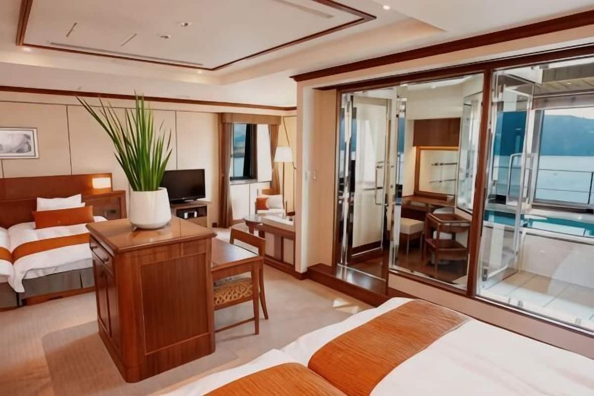 Habitación de hotel con cama, escritorio, silla, televisor y un ventanal con vista al mar.