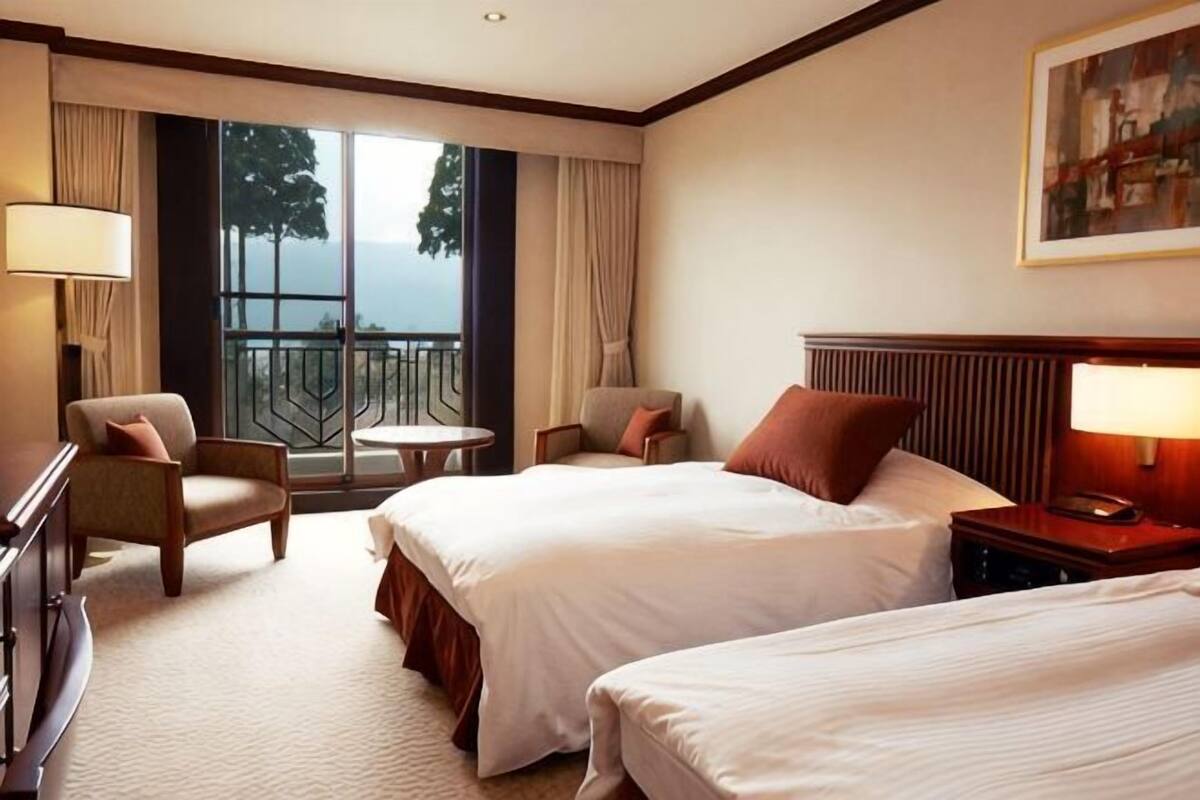 Habitación de hotel con dos camas, un escritorio, una silla, una mesita y un balcón con vistas.