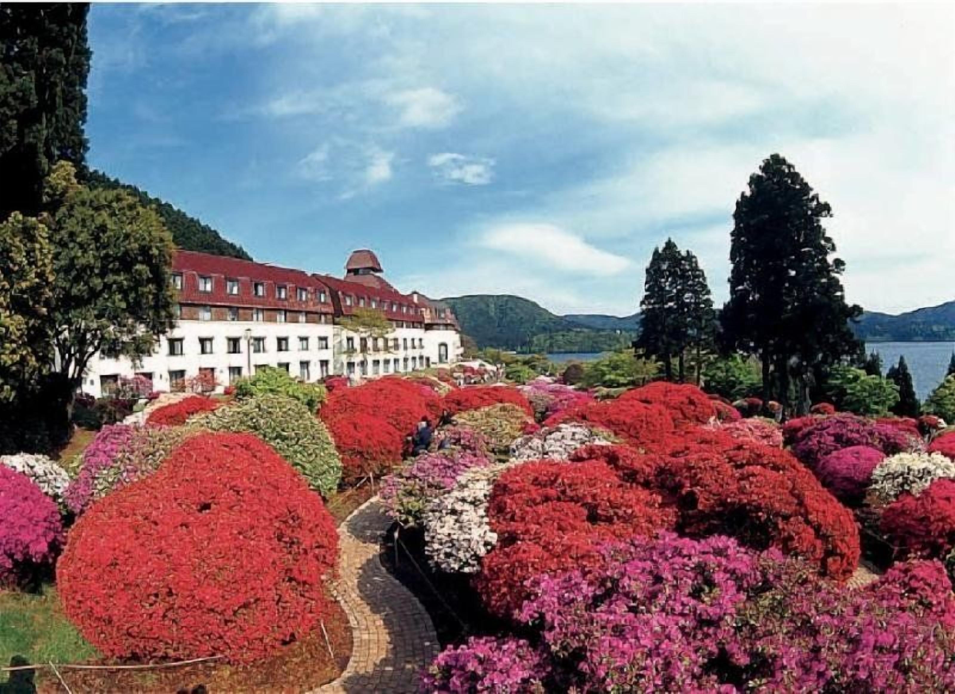 A large building with a red roof, surrounded by a garden with various colorful flowers.