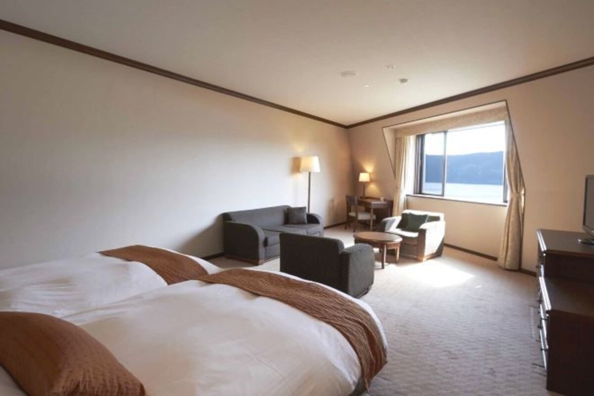 Habitación de hotel con dos camas, un sofá, una mesita y un televisor.