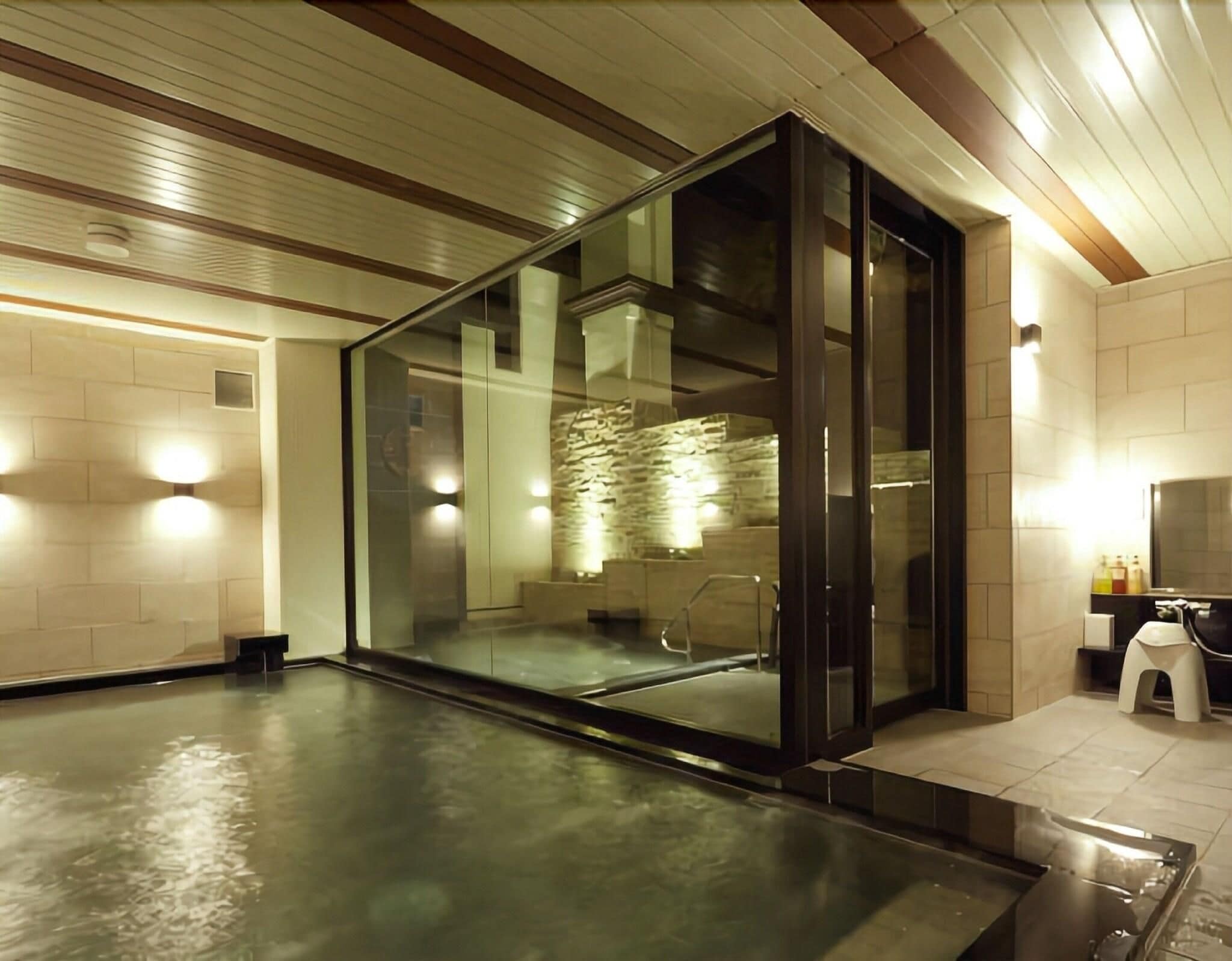 A modern bathroom with a glass enclosure, a stone wall, and a wooden ceiling.
