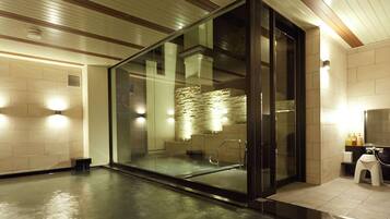 A modern bathroom with a glass enclosure, a stone wall, and a wooden ceiling.