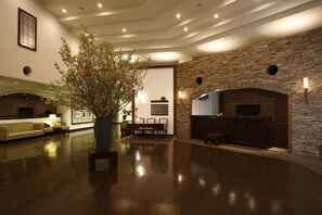 A spacious lobby with a stone fireplace, a seating area with a table and chairs, and a potted plant.