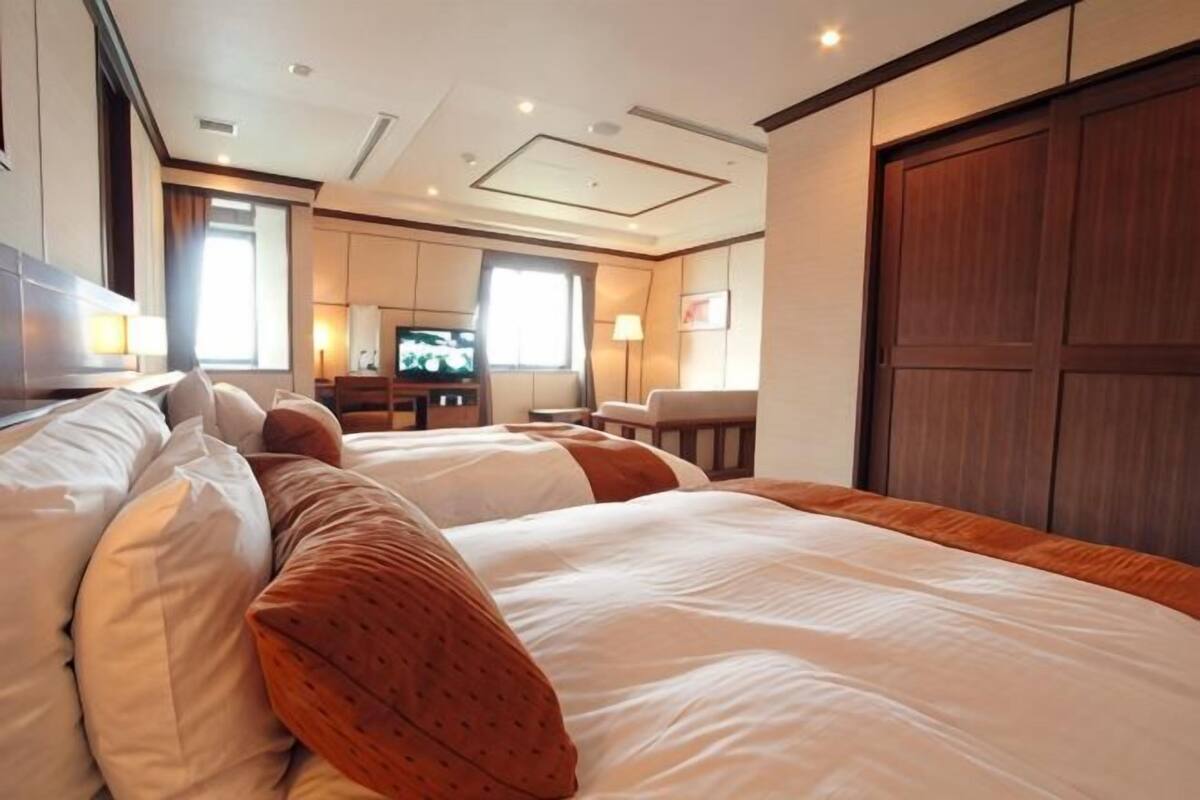 Habitación de hotel con dos camas, televisor, escritorio y un armario grande.
