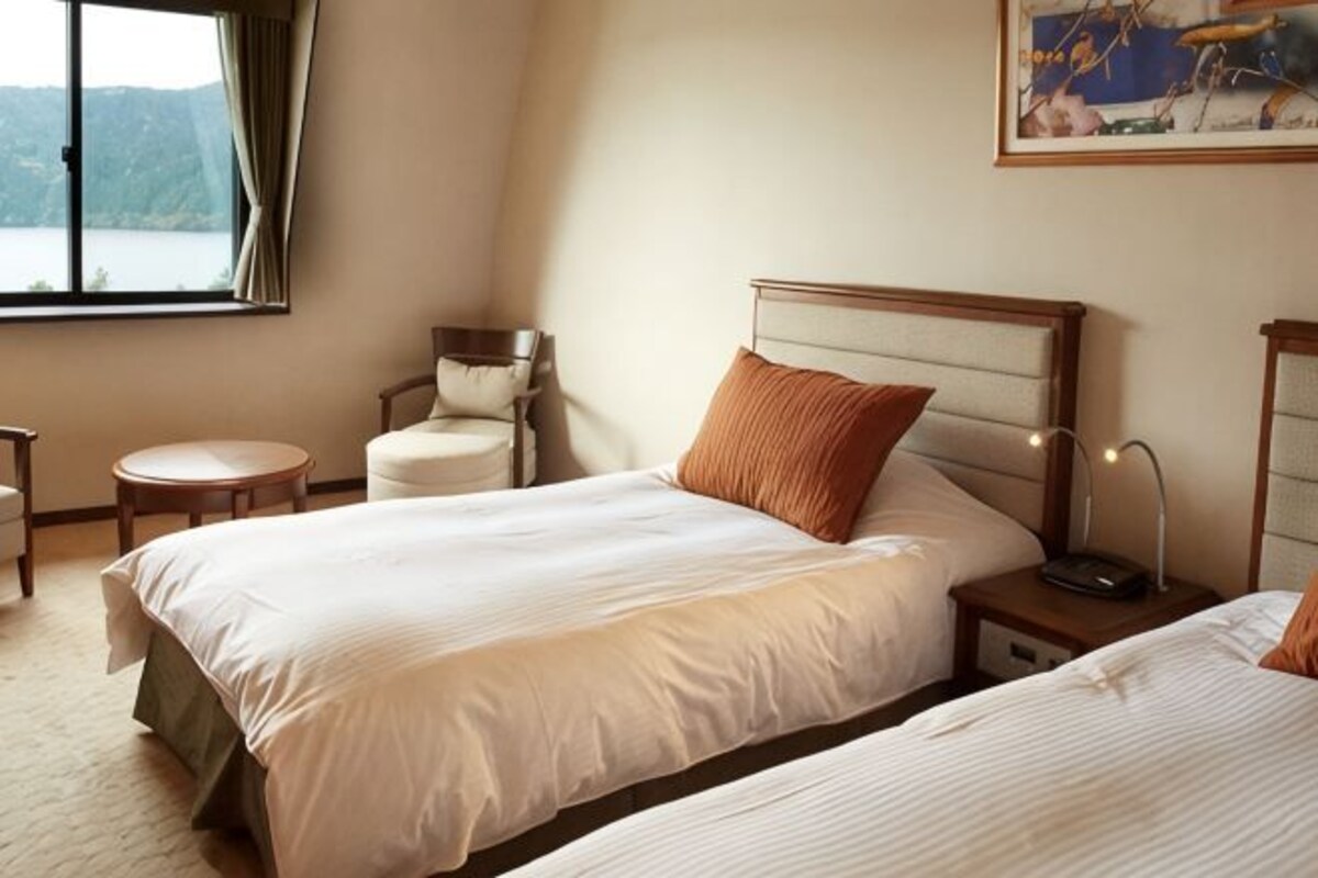 Habitación de hotel con dos camas, una silla, una mesa redonda y un cuadro en la pared.