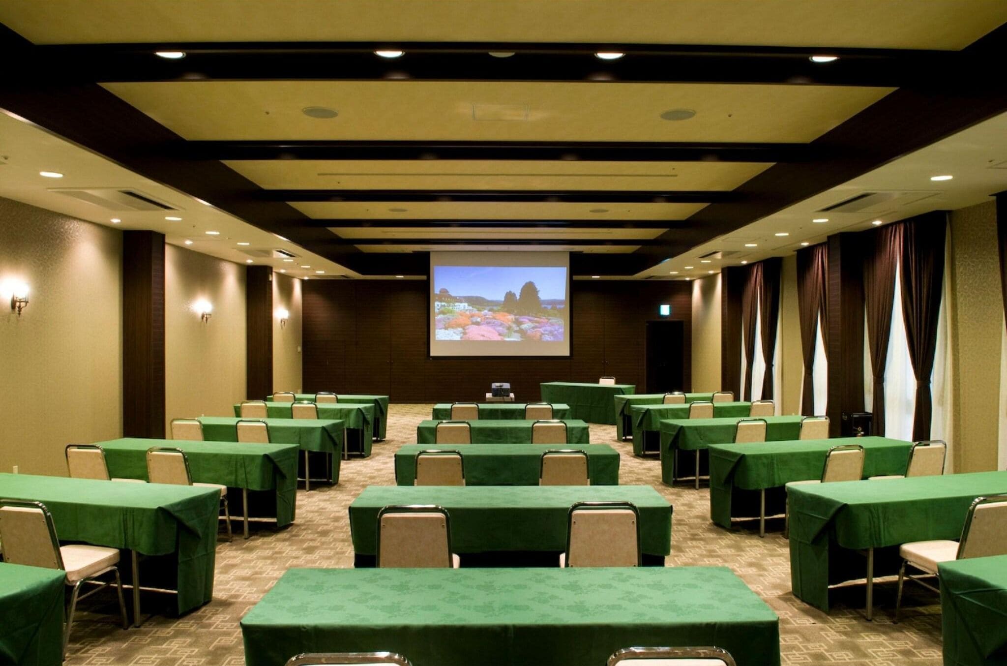 A conference room with multiple tables, a projector screen, and a carpeted floor.