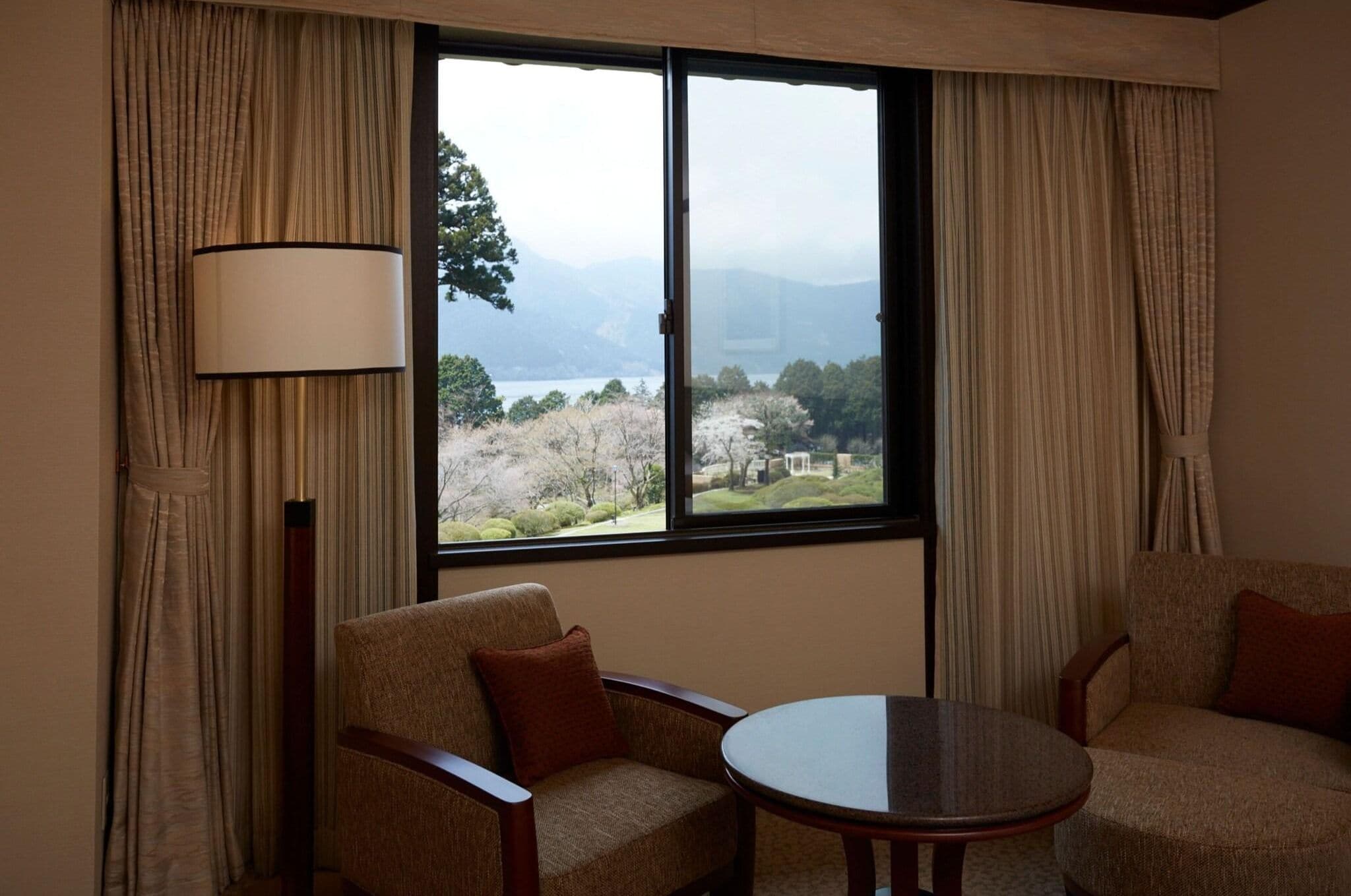 A room with two chairs, a table, and a large window with curtains.