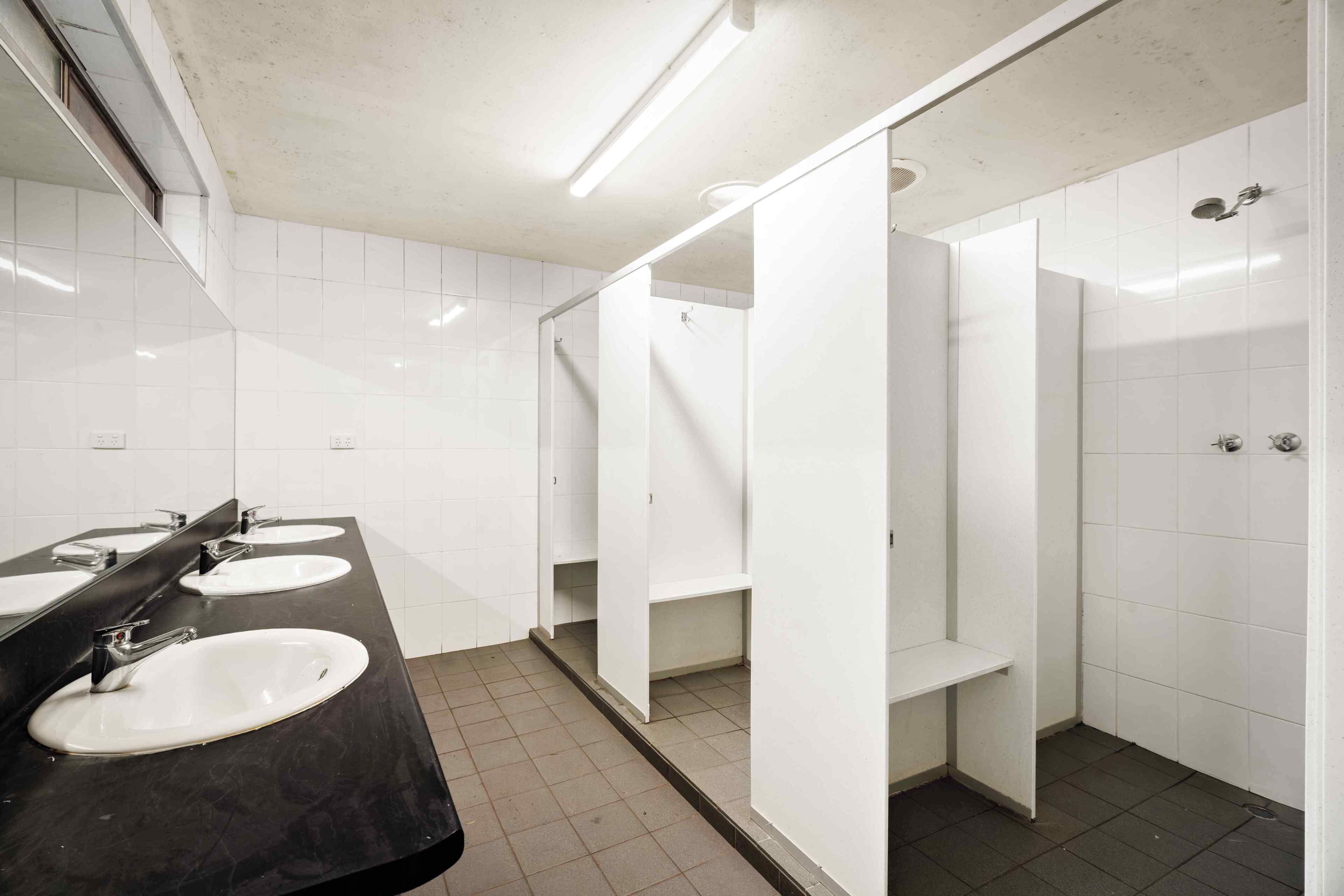 Casa de banho pública com três lavatórios, um espelho e área de duche.