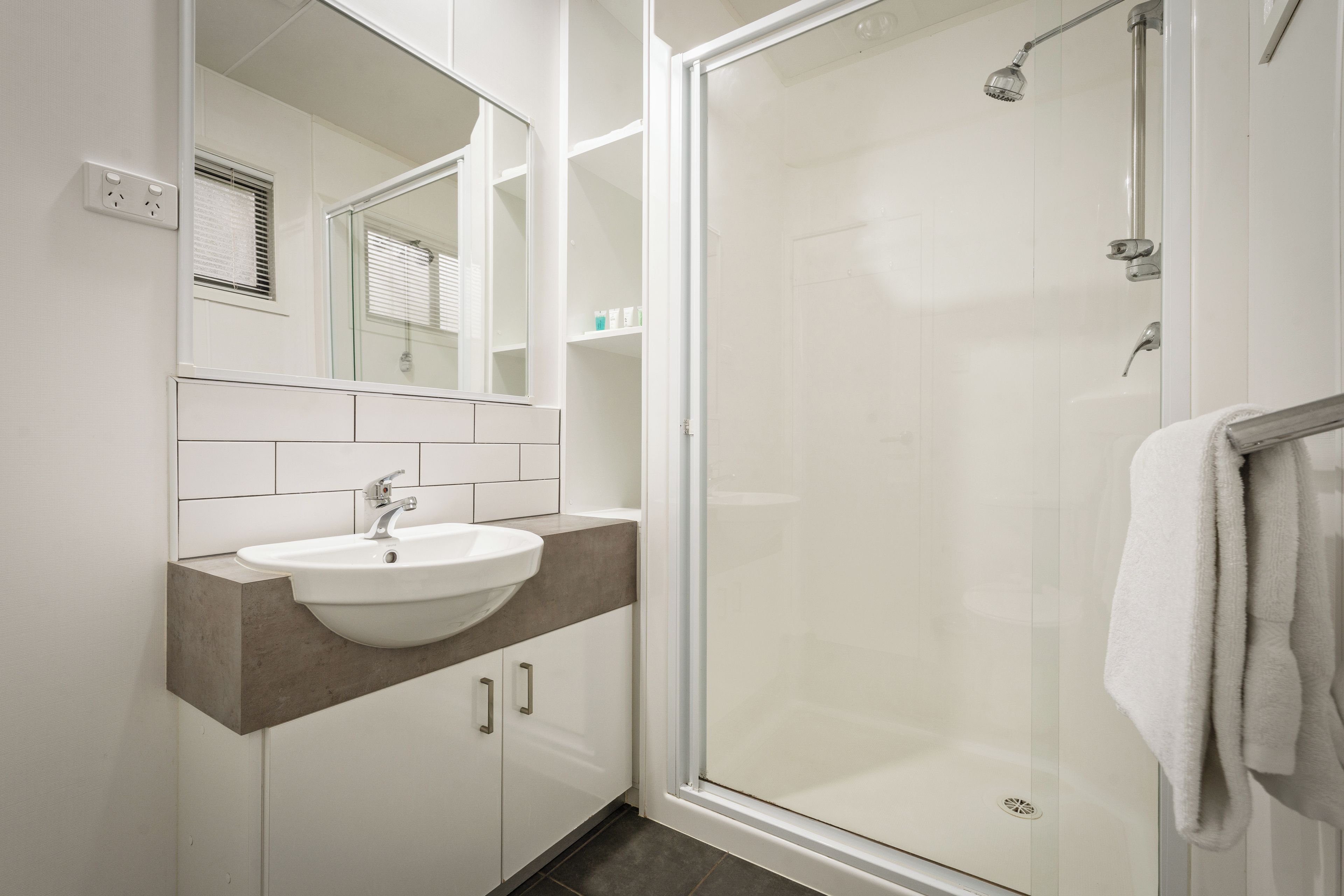 A modern bathroom with a glass-enclosed shower, a white sink, and a mirror above the sink.