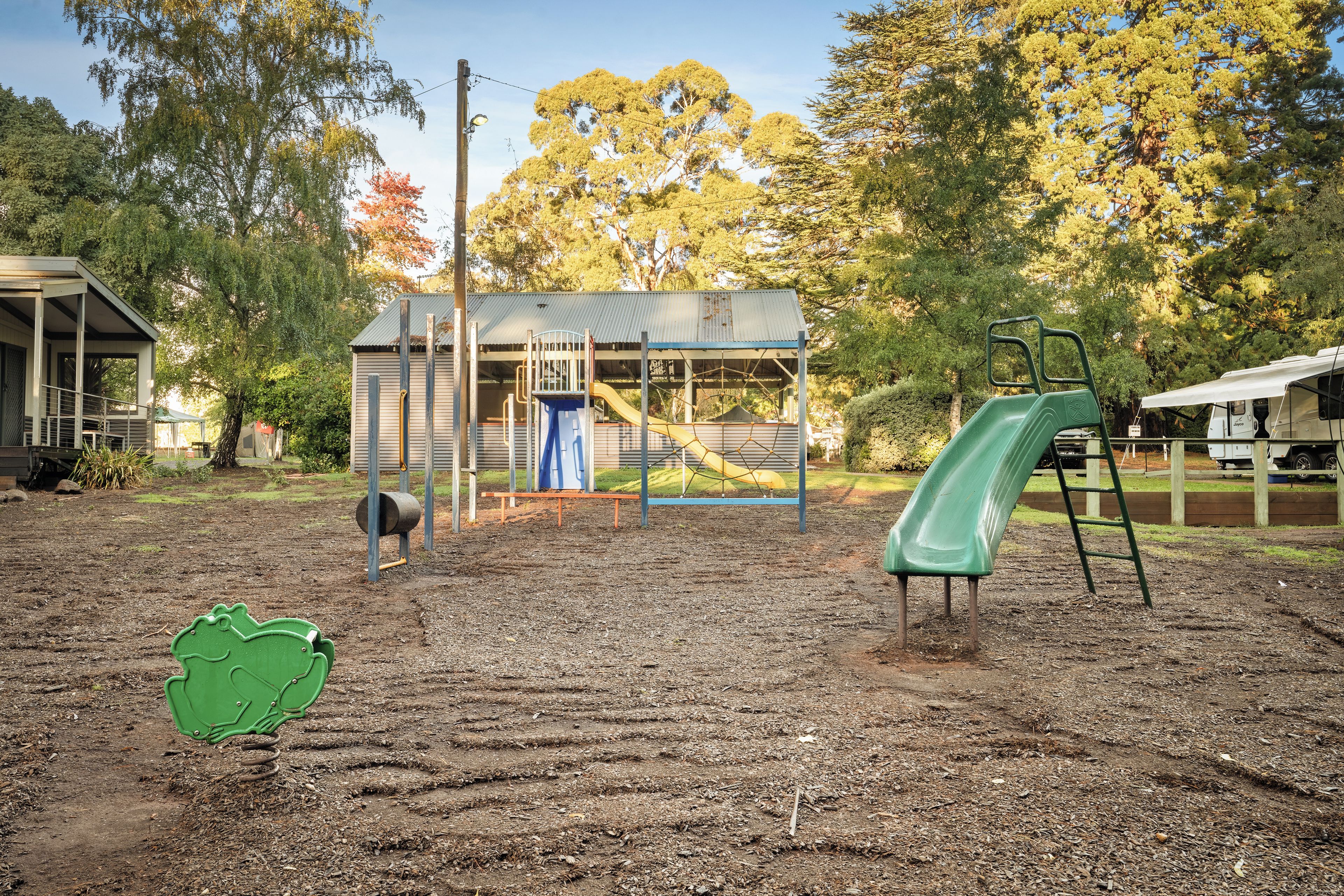 A playground with a slide and climbing structures, surrounded by trees and a building.
