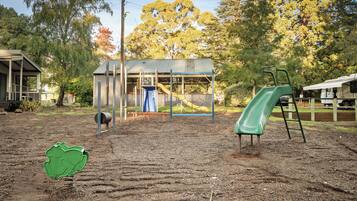 A playground with a slide and climbing structures, surrounded by trees and a building.