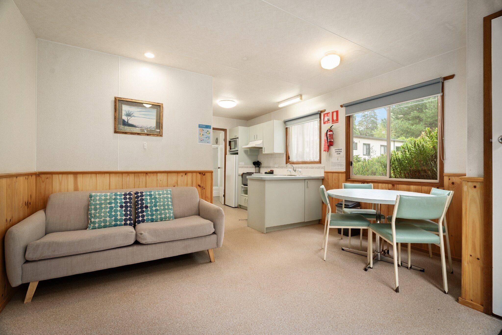 A compact living space with a sofa, dining table, chairs, kitchenette, and a window with a view.