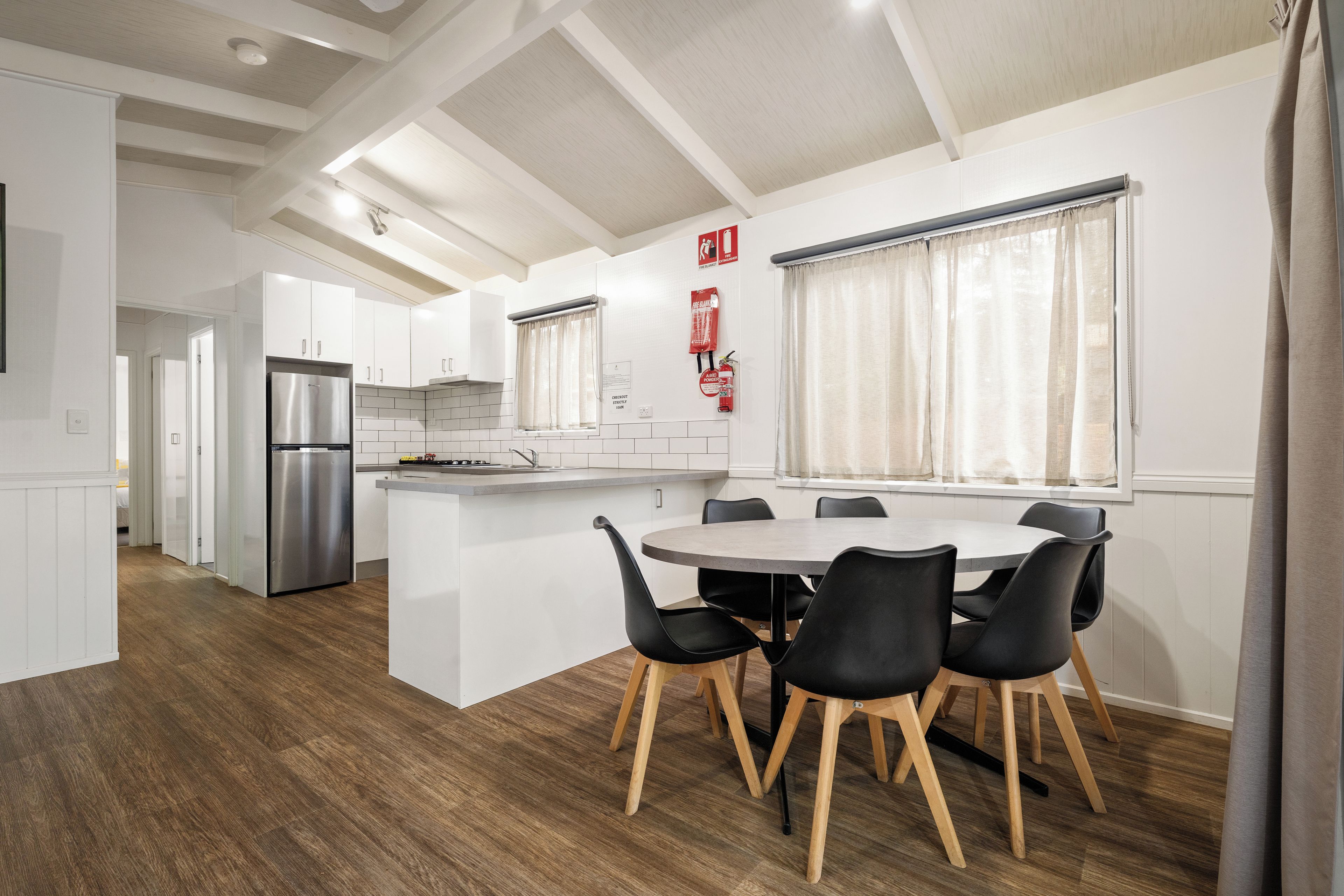 Una cocina moderna con armarios blancos, un refrigerador de acero inoxidable y un comedor con una mesa redonda y sillas negras.