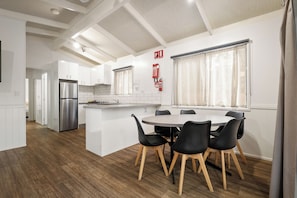 Une cuisine moderne avec des meubles blancs, un réfrigérateur en acier inoxydable et un coin repas comprenant une table ronde et des chaises noires.
