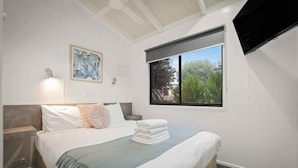 Une chambre à coucher comprenant un lit, une table de chevet, un téléviseur fixé au mur et une fenêtre donnant sur un paysage verdoyant.