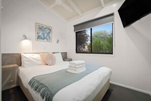 Une chambre à coucher comprenant un lit, une table de chevet, un téléviseur fixé au mur et une fenêtre donnant sur un paysage verdoyant.