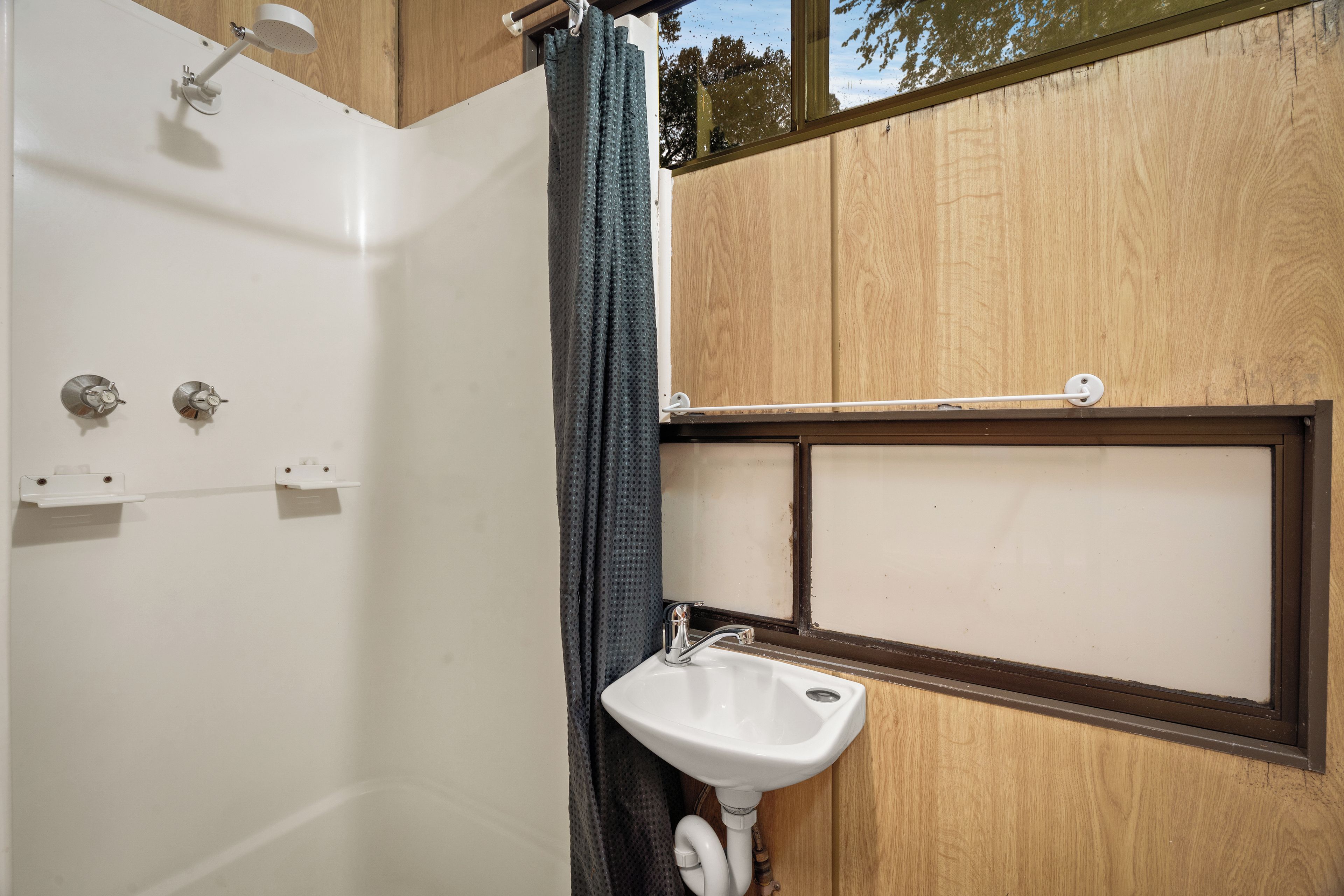 Een badkamer met een douche, een wastafel en een raam.