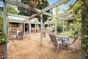 An outdoor patio area with tables and chairs, a brick building, and a pergola structure.