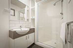 Une salle de bain moderne avec un lavabo blanc, une cabine de douche en verre et un miroir au-dessus du lavabo.